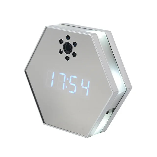 The Sleek Clock SpyCam features a hexagonal LED display, mirrored surface, and hidden spy camera lens on its face, surrounded by infrared night vision sensors.